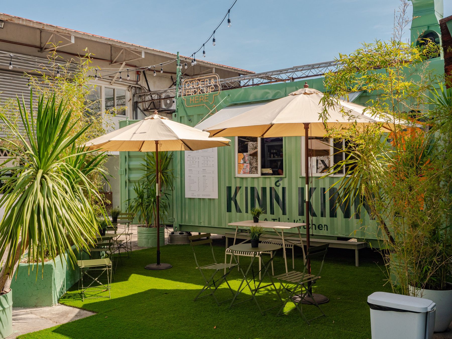 Kinn Kinn's green container kitchen in Camputhaw on a sunny day, with umbrellas, plants and string lights