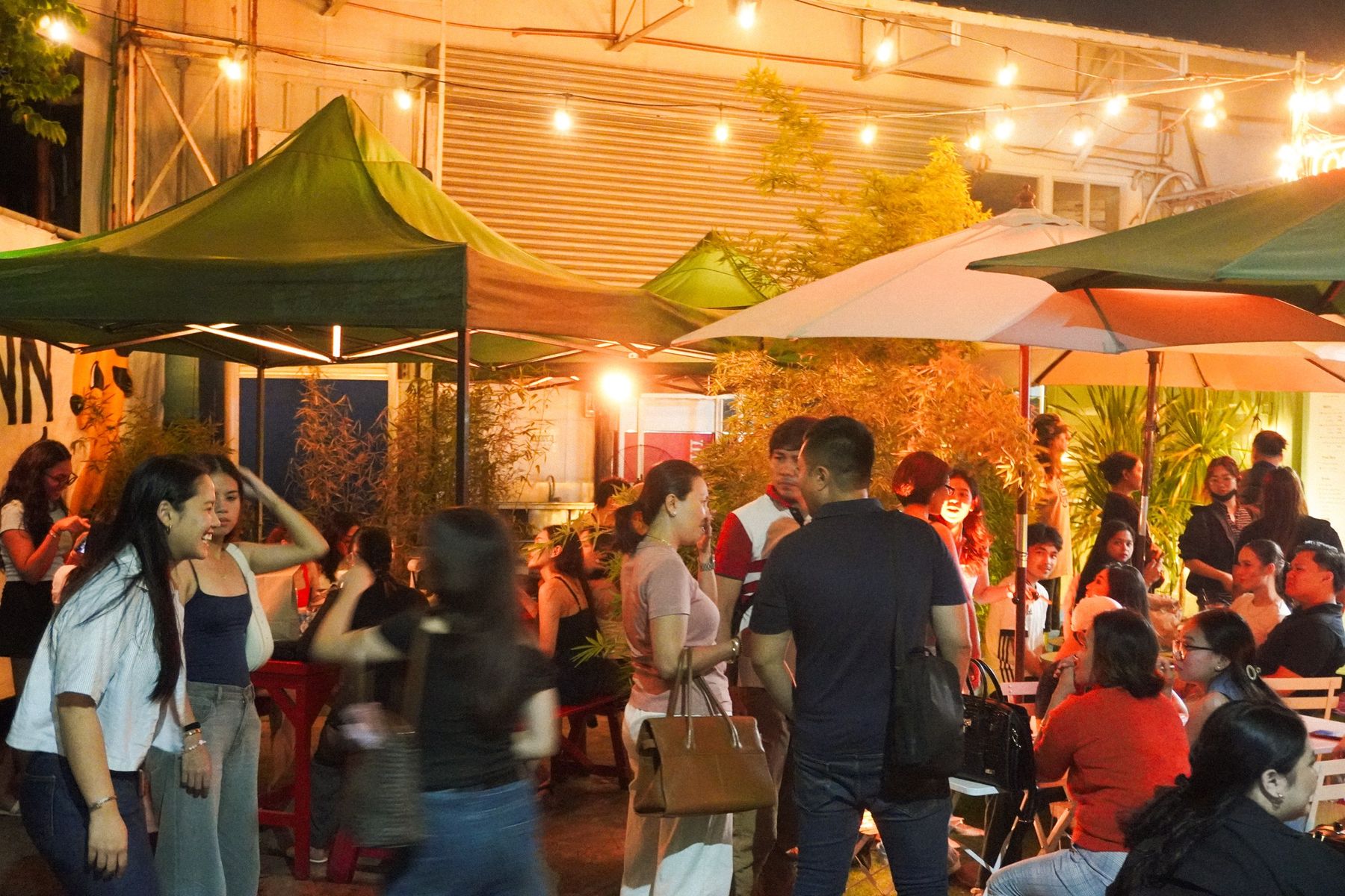 A crowd of friends eating and chatting under string lights at Kinn Kinn