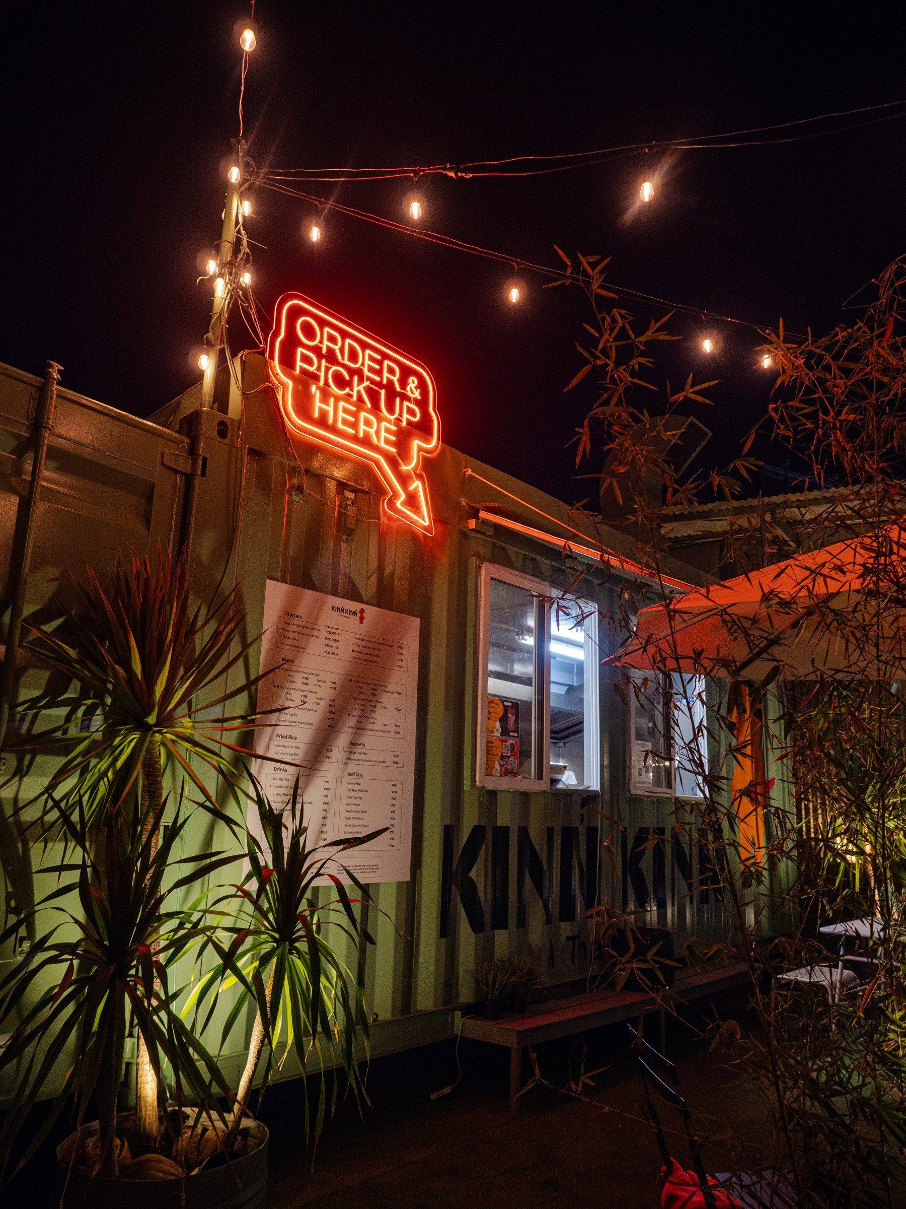 The Kinn Kinn container kitchen at night, with its orange neon Order and Pick up here sign and string lights overhead